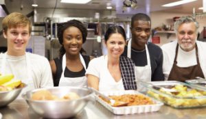 Diverse group of volunteers in kitchen smiling with meal they all helped to prepare